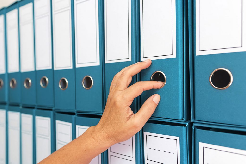 Rows of blue binders with a hand reaching to pull one out.